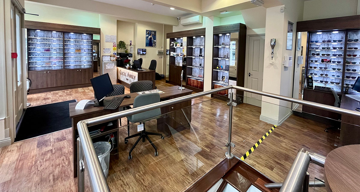 The dispensing floor at Cecil Amey Opticians Norwich, walnut joinery and lit glass cabinets stocked with Chanel, Lindberg and Tom Ford